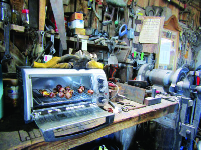 A toaster oven full of chestnuts on a table covered in blacksmithing tools.